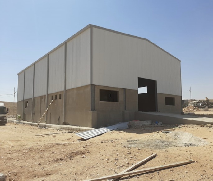 مستودع بهيكل حديدي وكسوة معدنية قيد الإنجاز في موقع صحراوي من تنفيذ مقاولات E&M — steel-framed warehouse with metal cladding built by E&M