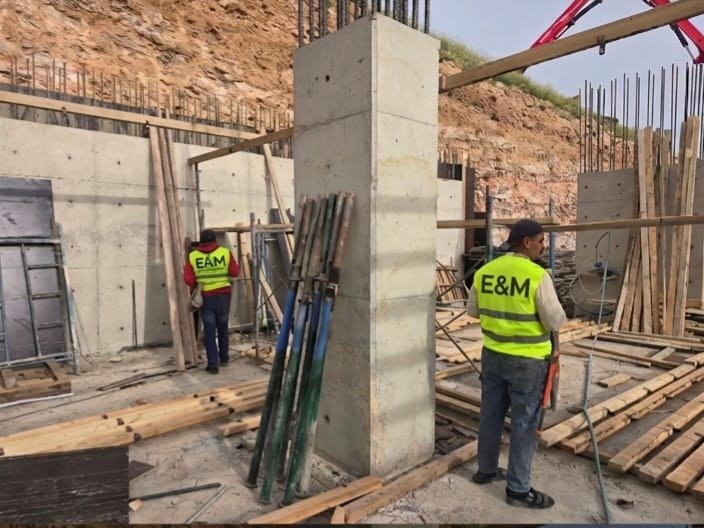 E&M site crew in branded safety vests beside a completed reinforced concrete column