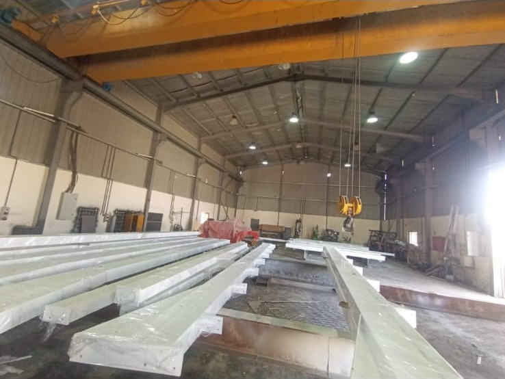 جوائز حديدية مدهونة داخل ورشة تصنيع E&M تحت رافعة جسرية — painted steel beams inside the E&M fabrication workshop